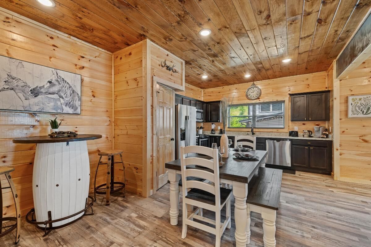 A wooden cabin interior with a dining area, kitchen, and a clock on the wall.