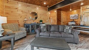 Ein Holzblockhaus-Interieur mit Sofa, Sessel und Couchtisch, Holzwänden und einem Essbereich.