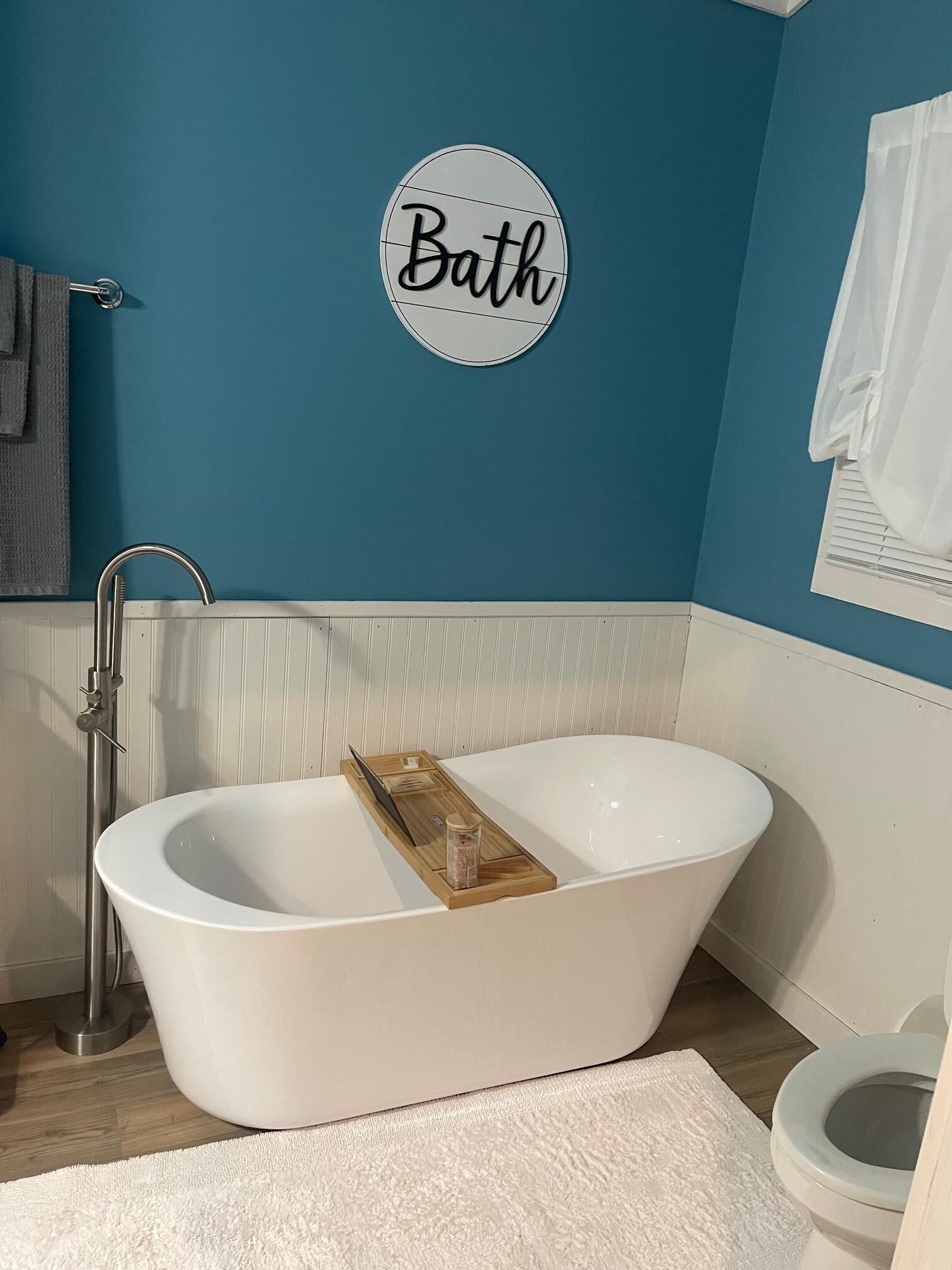 A bathroom with a freestanding bathtub, a towel rack, a toilet, and a wall-mounted sign that reads 'Bath'.