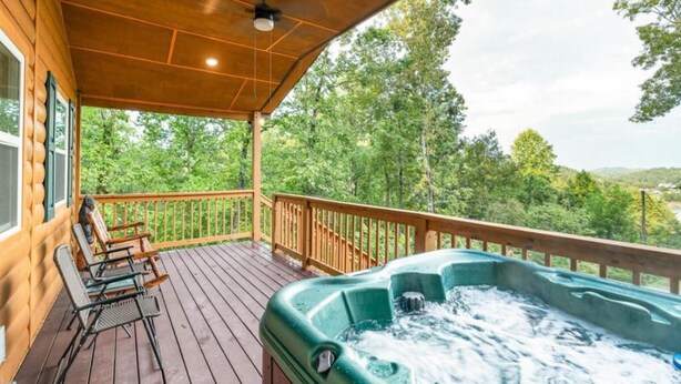A wooden deck with a hot tub, outdoor seating, and a view of trees and hills. - Cozy Hollow Cabin (Sevierville)