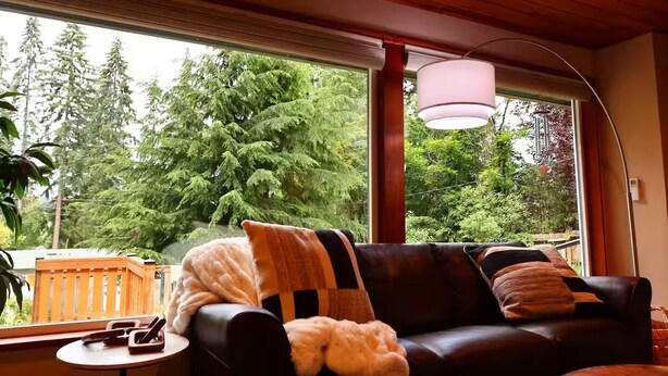 Ein gemütliches Wohnzimmer mit Ledersofa, einem runden Tisch und einem großen Fenster mit Blick auf Bäume.
