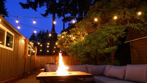 Eine Terrasse im Freien mit Feuerstelle, Lichterketten und Holzzaun.