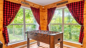 Una stanza in legno con un tavolo da calcio, ampie finestre con tende rosse e un cartello che riporta 'Great Smoky Mountains'.