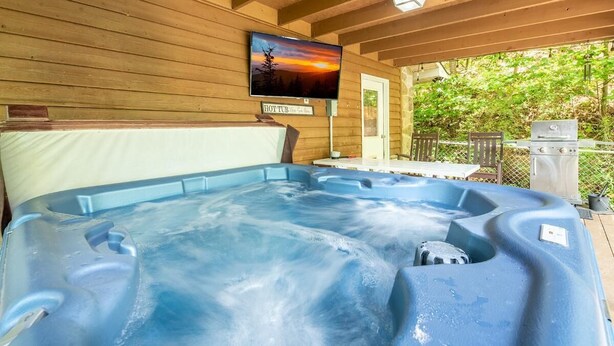 Una vasca idromassaggio con un pontile in legno, un televisore montato a parete e un cartello con la scritta 'HOT TUB'.