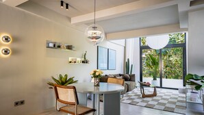 A modern living room with a dining area, large windows, and a view of greenery.