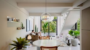 A modern interior with a dining area, a sofa set, and a large window with a view.