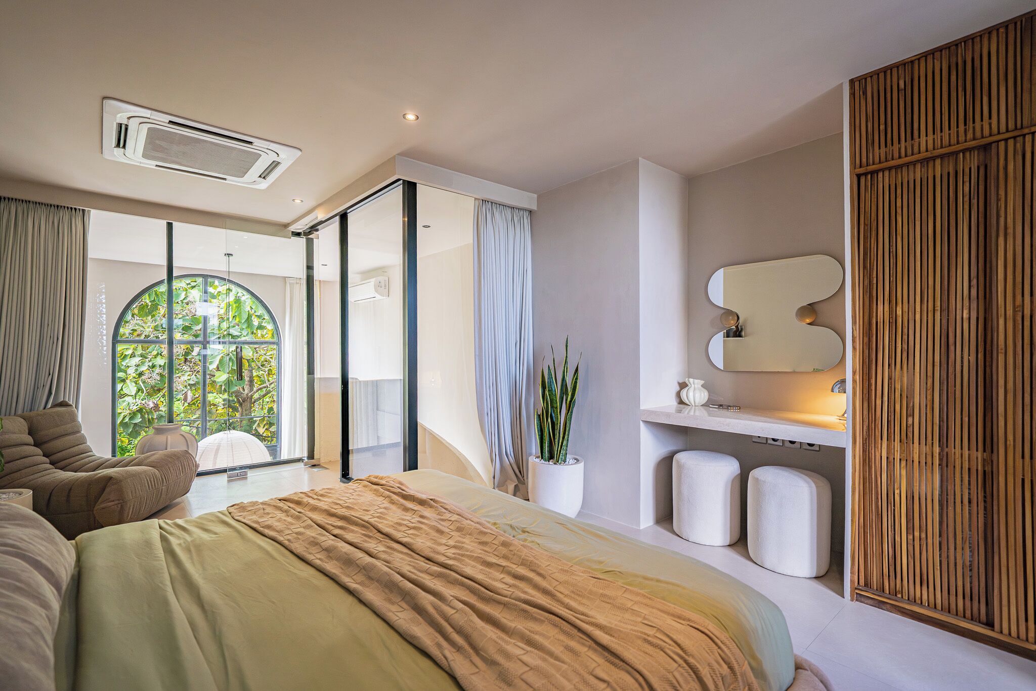 A modern bedroom with a large bed, a sliding glass door leading to a balcony, a wall-mounted mirror, and a wooden panel wall.