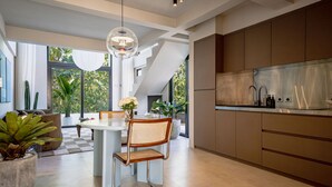 A modern kitchen with a dining area, large windows, and a view of greenery.