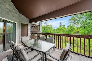 A balcony with a glass table and chairs, a door, and a view of greenery. - Gracious Oasis (Gatlinburg)