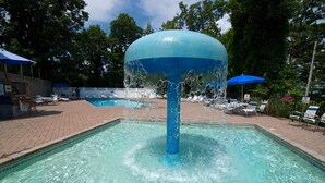 Una piscina con fuente de agua, sillas de descanso y sombrillas.