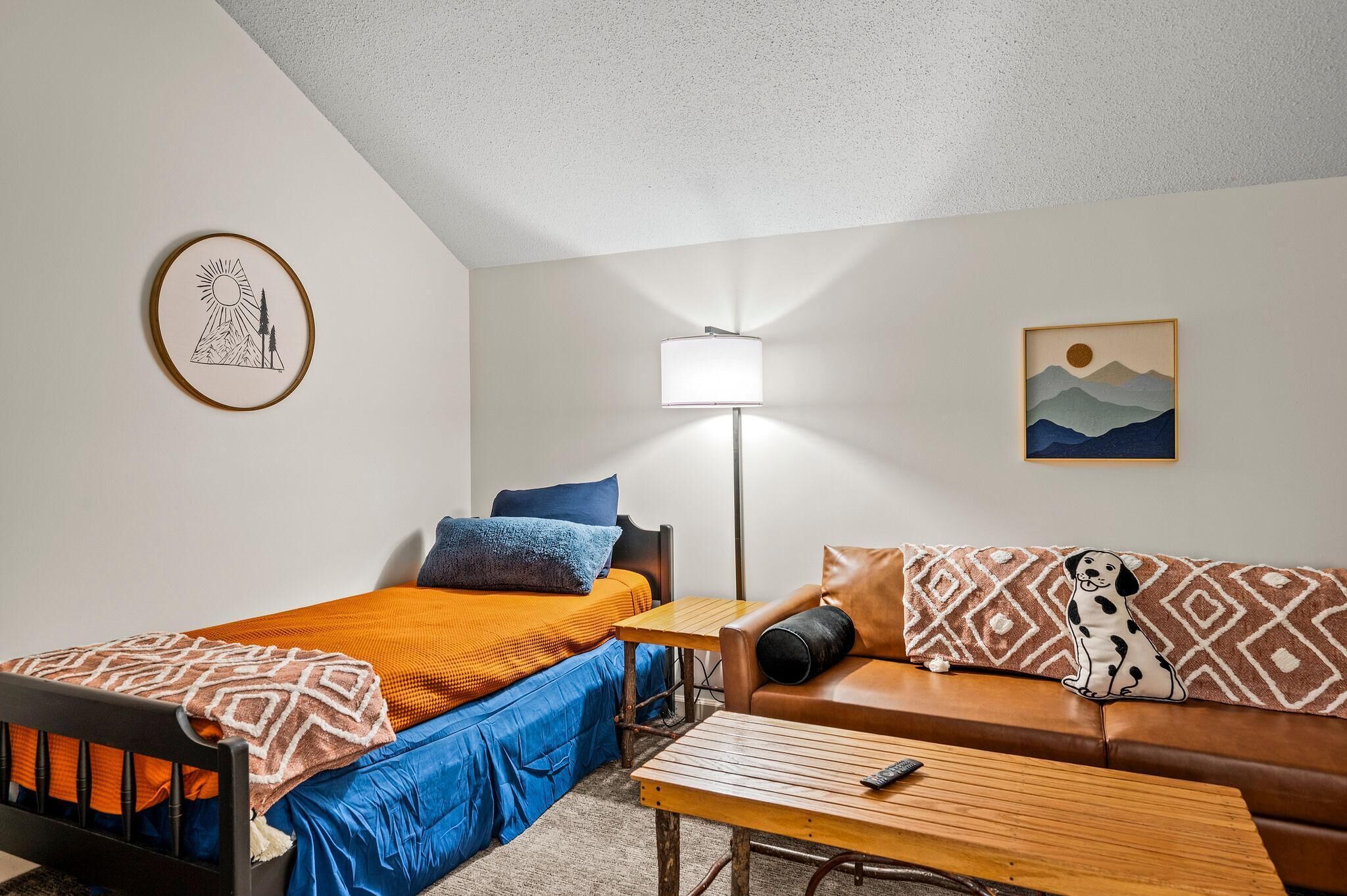 A room with a bed, a sofa, a lamp, and a small table.