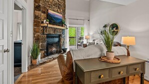 Una sala de estar con chimenea de piedra, un sofá, una mesa con cajones y vistas al exterior.