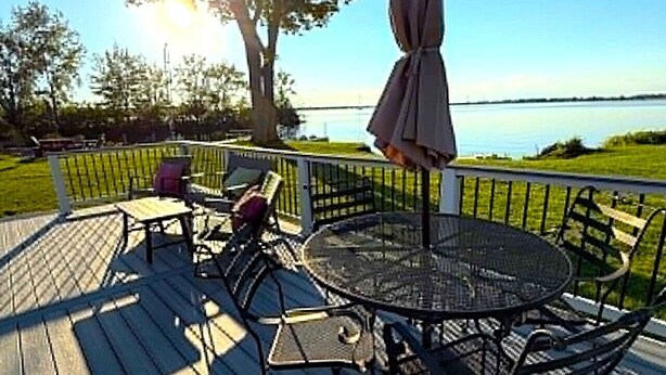 Una terraza con una mesa redonda y sillas, un paraguas y vistas a un cuerpo de agua.