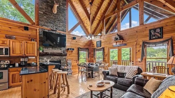 A cabin with a kitchen, dining area, and living room, featuring wooden walls, large windows, and a stone fireplace. - Away in the Mountains (Sevierville)