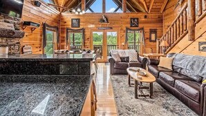 A log cabin interior with a kitchen, living area, and a staircase. - Away in the Mountains (Sevierville)