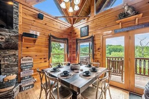 Ein Holzblockhaus-Interieur mit einem für vier Personen gedecktem Esstisch, einem Kamin und einem herrlichen Ausblick durch die Fenster.