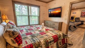 Um quarto acolhedor com cama, janela com persianas, televisão na parede, escrivaninha com computador e mesa de bilhar.