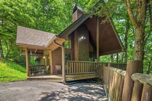 Eine Hütte mit überdachter Veranda, einer kleinen Terrasse und Blick auf den umliegenden Wald.