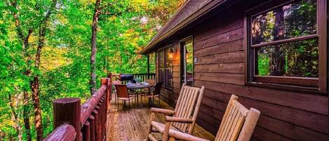 A wooden cabin with a porch, outdoor seating, and a view of a forest.