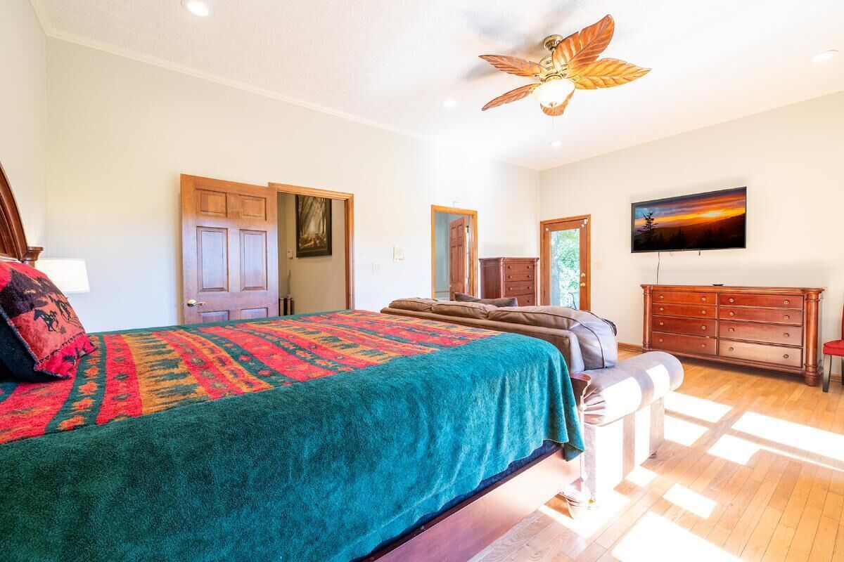 A bedroom with a bed, a ceiling fan, a dresser, a television, and a door.