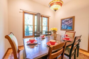 A dining area with a wooden table set for four, two windows with curtains, a vase with yellow flowers, and a framed painting on the wall. - Peachtree (Sevierville)