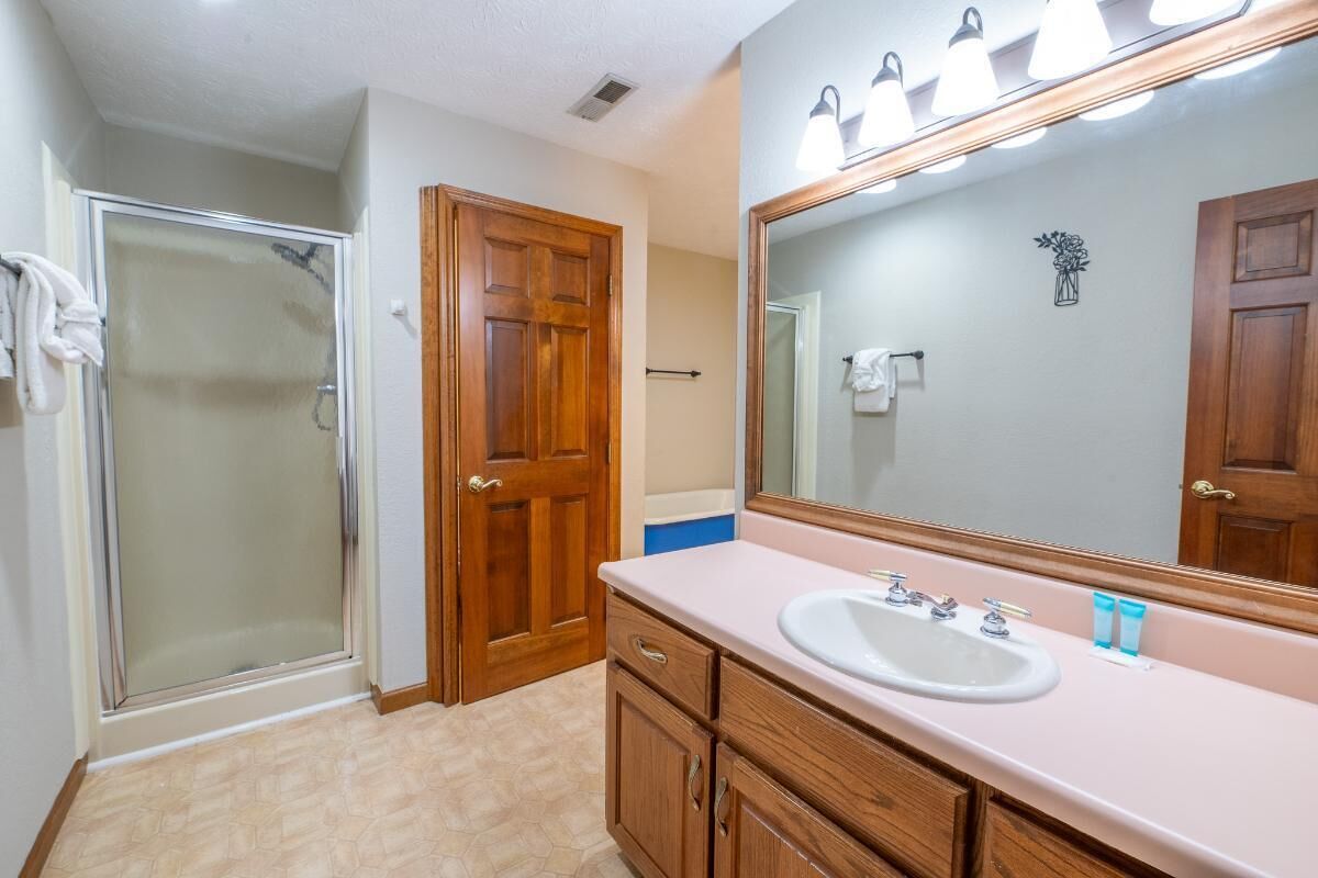 A bathroom with a shower, a sink, wooden cabinets, and a large mirror.