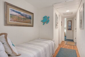 Ein Schlafzimmer mit einem Bett, einem gerahmten Landschaftsbild, einer Schildkrötendekoration und einem Flur, der in ein weiteres Zimmer führt.