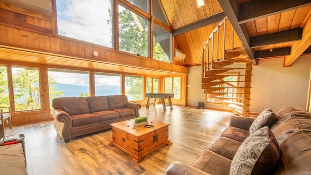 Ein geräumiger Raum mit einer großen Holztreppe, einem Ledersofa, einem Holztisch und großen Fenstern mit Blick ins Freie.