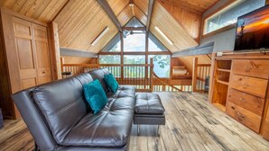 Ein Zimmer mit hohen Decken, einer Holzbalkendecke, einem Ledersofa, einem Holztisch und einem großen Fenster.