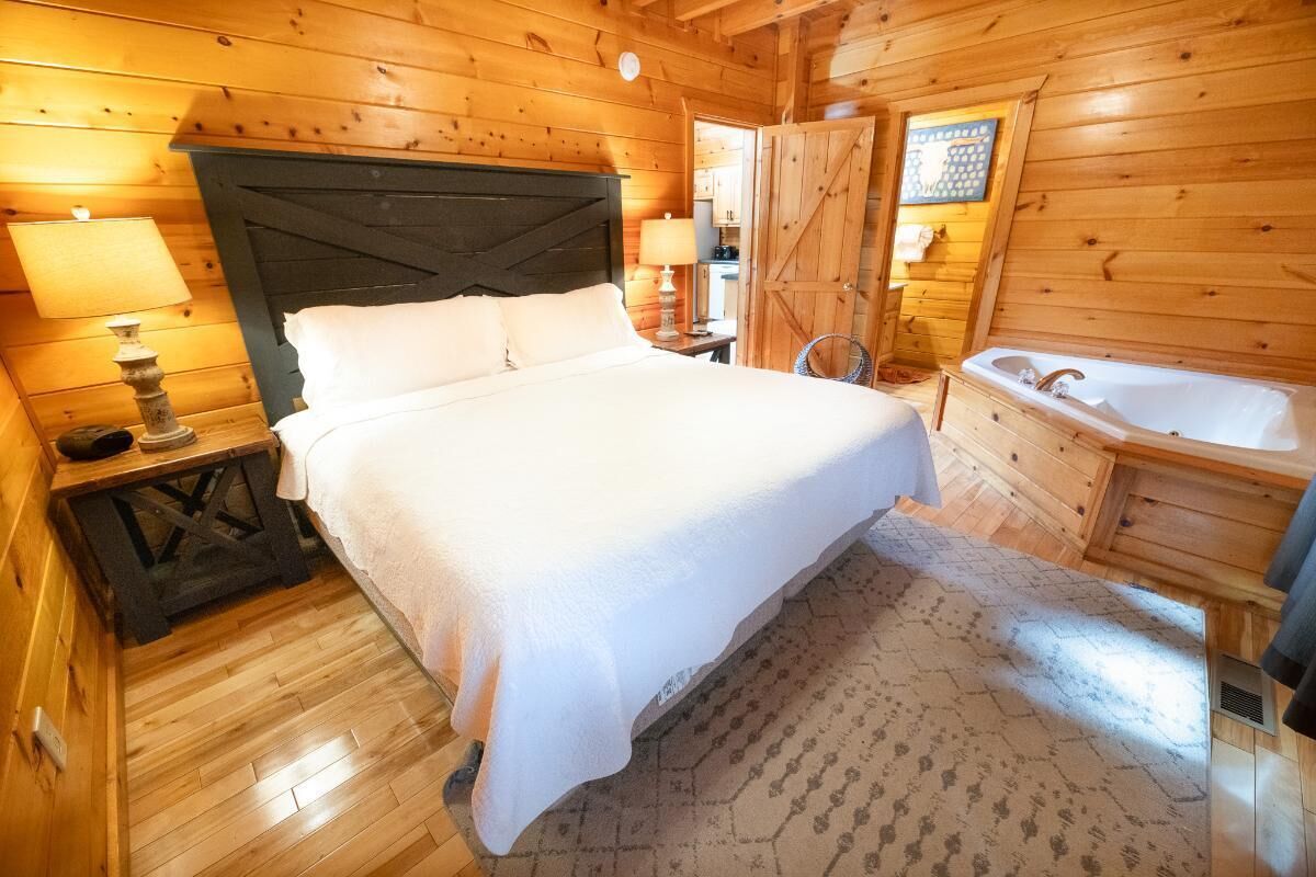 Une chambre à coucher dans un chalet en bois, avec un lit, des lampes de chevet, un tapis et une salle de bain équipée d’une baignoire.