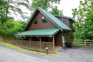 Eine Blockhütte mit Veranda, einem grünen Dach und einem Holzzaun.