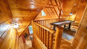 Puinen mökki, jonka sisustuksessa on biljardipöytä, puiset kaiteet ja portaikko.