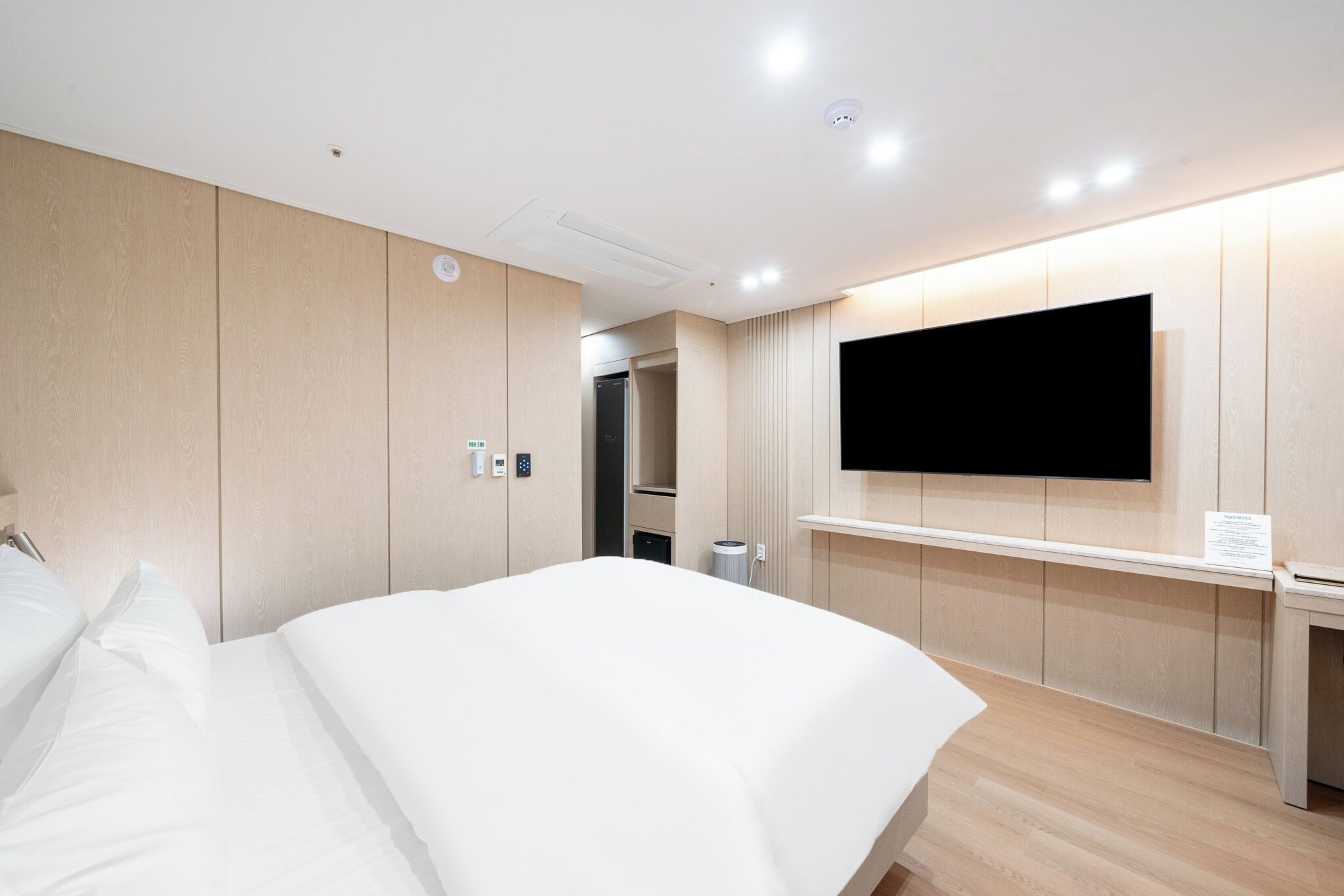 A hotel room with a bed, a TV mounted on the wall, a desk, and a door leading to a bathroom.