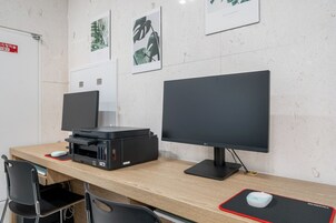 Una oficina moderna con dos monitores, una impresora y un escritorio con sillas.