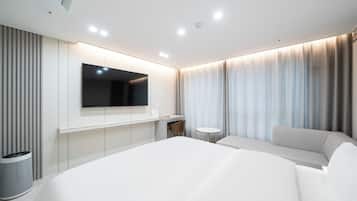 Une chambre d’hôtel moderne dotée d’un grand lit, d’un téléviseur à écran plat fixé au mur, d’une petite table ronde et d’un coin salon avec un canapé.