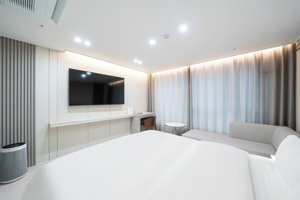 A modern hotel room with a large bed, a flat-screen TV mounted on the wall, a small round table, and a seating area with a sofa. - Zenith Hotel (Jecheon)