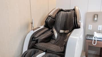 A massage chair with a control panel, a desk with a telephone, and a wall-mounted light fixture.