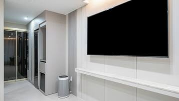 A modern hotel room with a large flat-screen TV mounted on the wall, a glass partition, and a small trash bin.