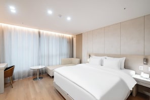 Una habitación de hotel moderna con una cama grande, una mesita redonda pequeña, una silla y un escritorio.