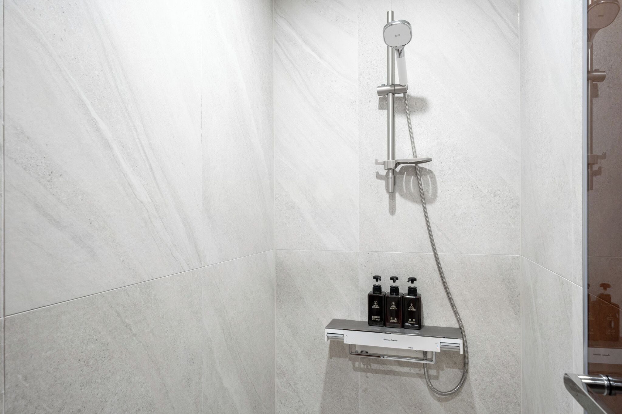 Un baño moderno con ducha, dispensador de jabón de pared y cabezal de ducha de mano.