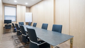 Un salón de conferencias con una mesa larga, seis sillas, una pizarra y un monitor de computadora.