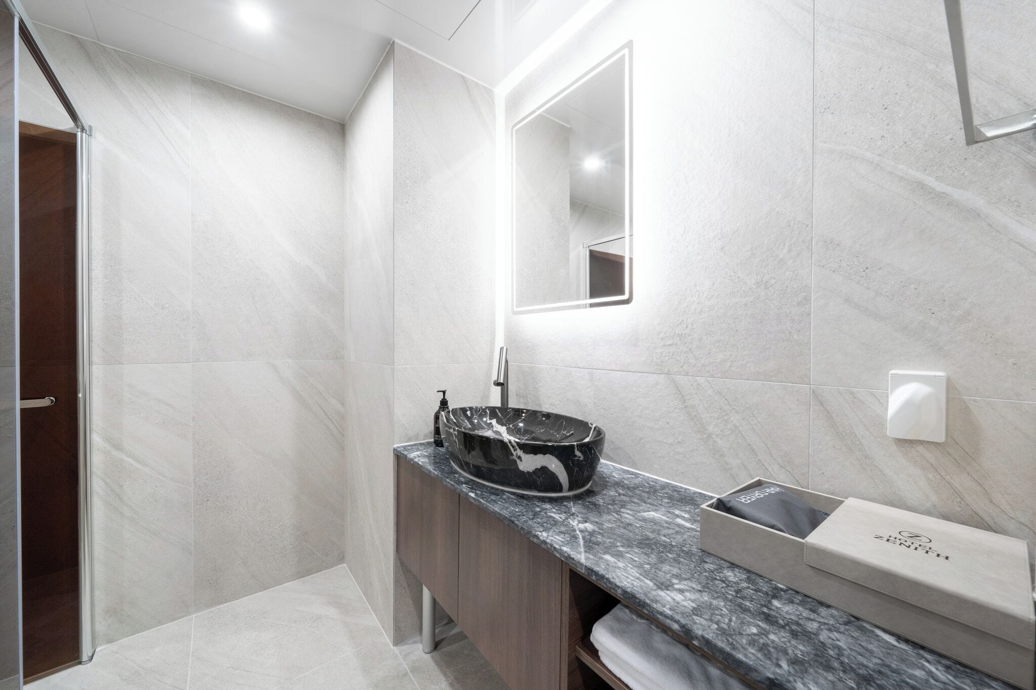 A modern bathroom with a marble sink, a glass shower enclosure, and a built-in mirror.