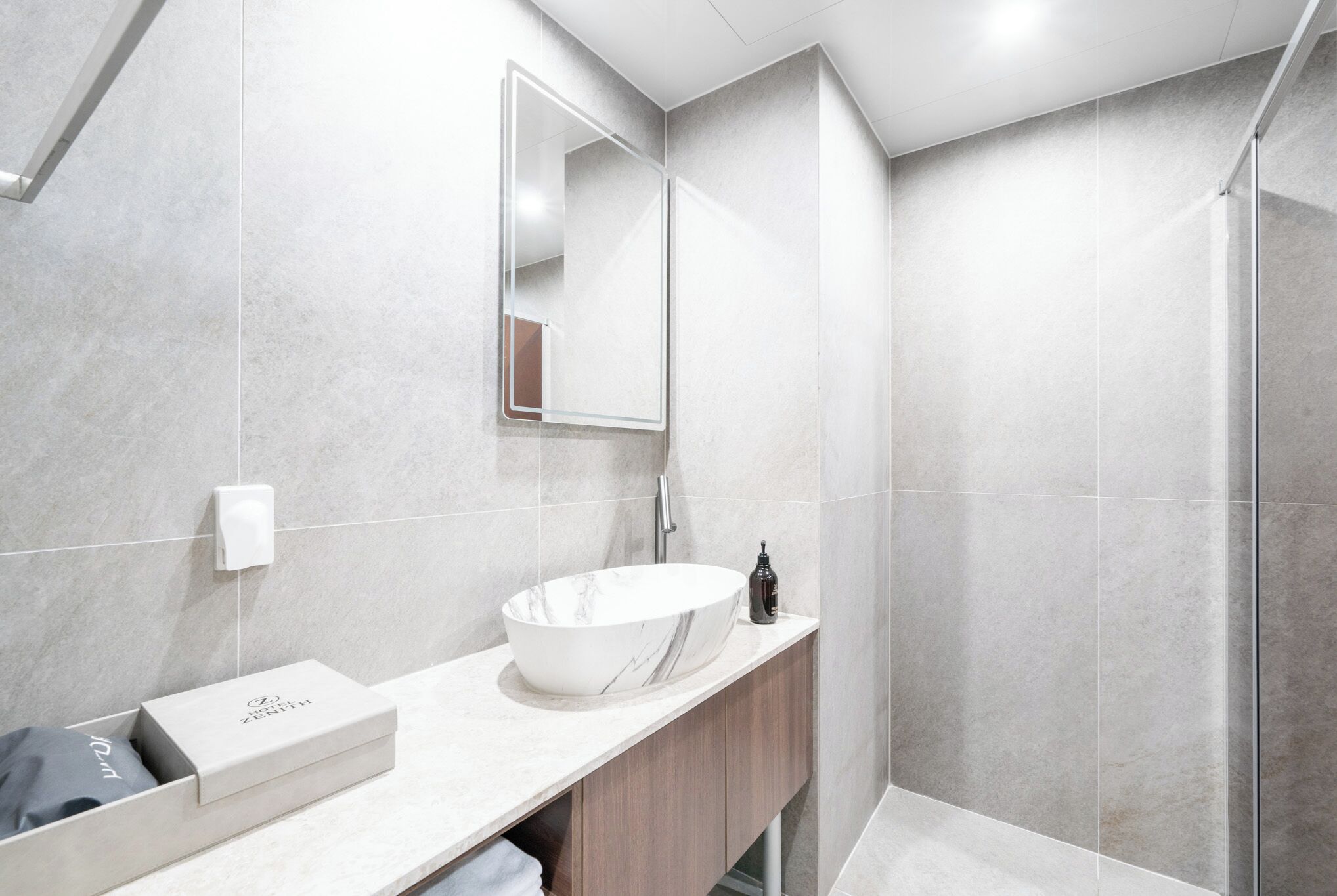 A modern bathroom with a large white sink, a mirror, and a shower area.