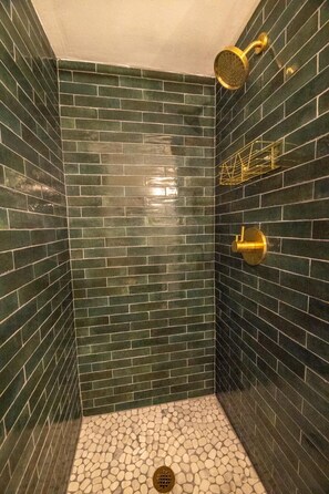 Eine Dusche mit Regendusche und Handbrause, geflieste Wände und ein Boden mit Kieselsteindekor.