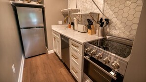 A compact kitchen with a refrigerator, oven, microwave, and a countertop with utensils. - Enchanted Treehouse Hideaway (Gatlinburg)