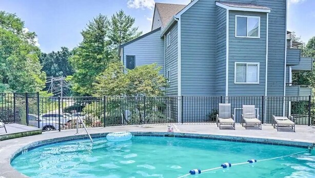 A swimming pool with a fence, lounge chairs, and a building in the background. - Enchanted Treehouse Hideaway (Gatlinburg)