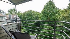A balcony with a metal railing, a chair, and a view of a forested area. - Enchanted Treehouse Hideaway (Gatlinburg)