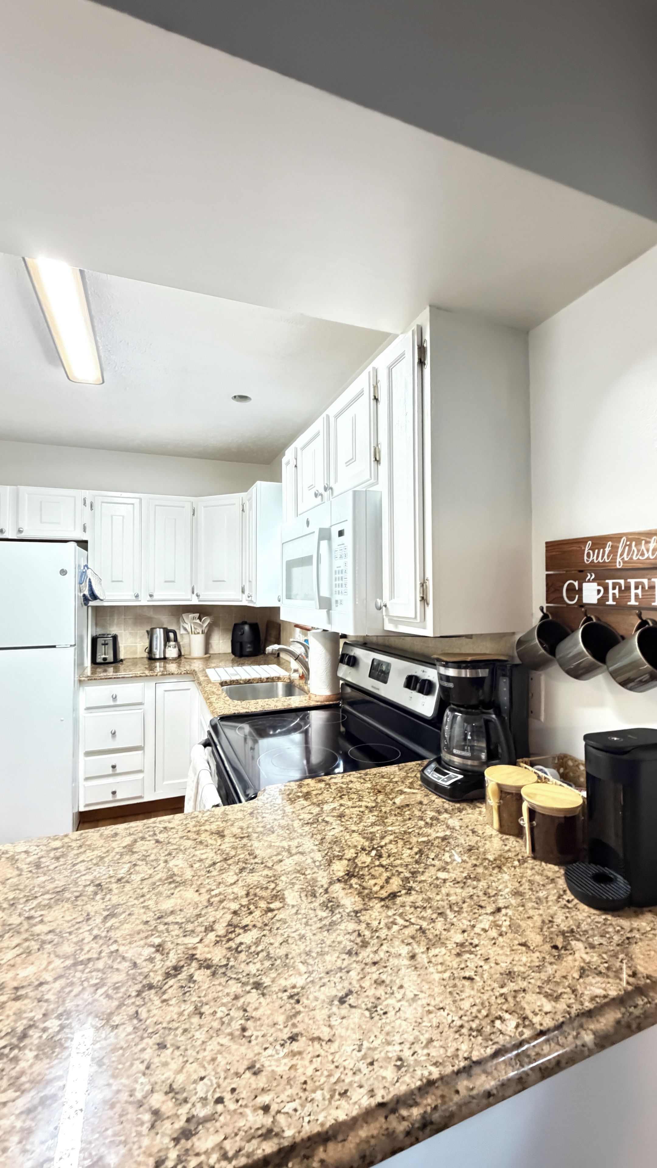 A kitchen with white cabinets, a granite countertop, a microwave, a stove, and a coffee station.