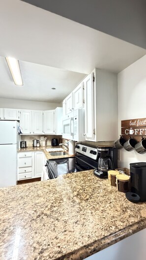 A kitchen with white cabinets, a granite countertop, a microwave, a stove, and a coffee station. - Arcade + Fire Pit + Pet-Friendly + Pocono Cabin (Tobyhanna)
