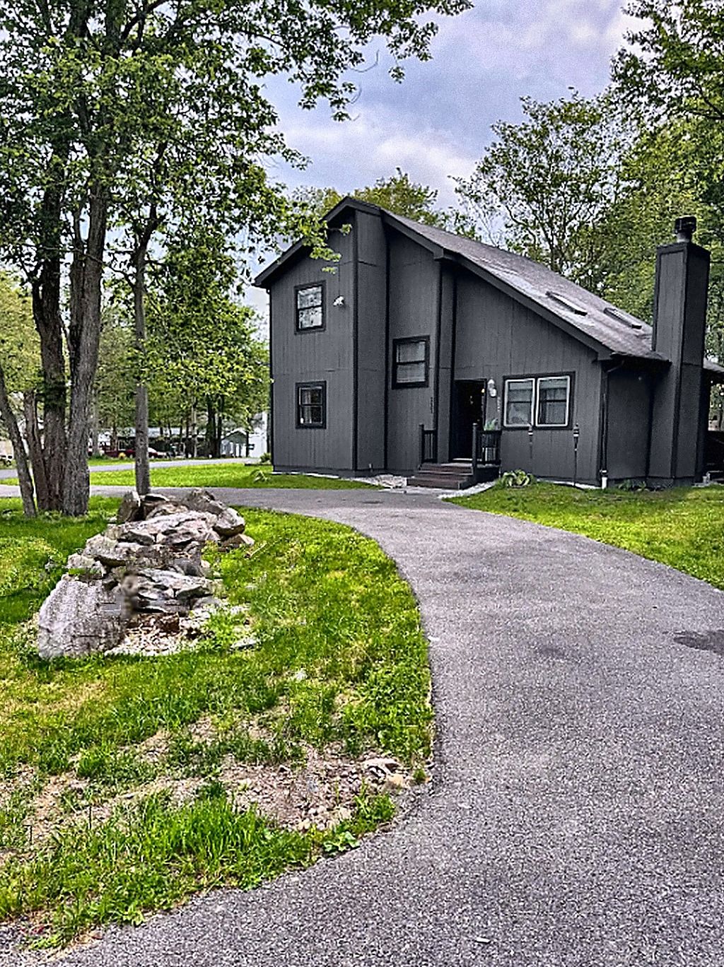 A two-story building with a dark exterior, a driveway leading to the entrance, and a grassy area with rocks.
